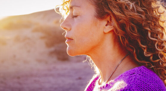 Close up sunset portrait of attractive woman with closed eyes and sun in back light. Dreaming and enjoying feeling concept lifestyle emotion. Serene female people outdoor with curly hair