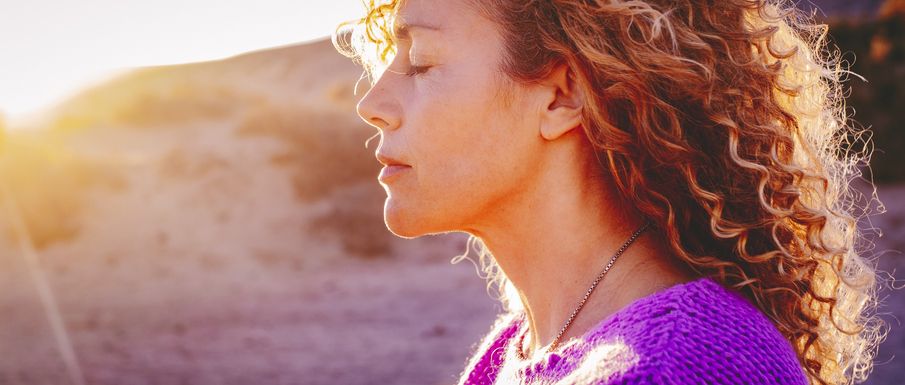 Close up sunset portrait of attractive woman with closed eyes and sun in back light. Dreaming and enjoying feeling concept lifestyle emotion. Serene female people outdoor with curly hair